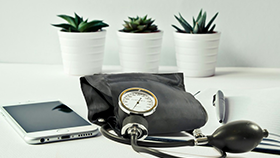 A blood pressure monitor sitting on a desk, next to a tablet device and a pen.